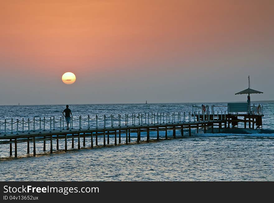 The person on a pier during sunrise on the sea