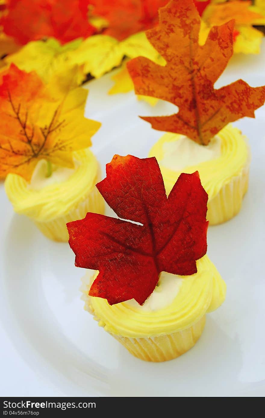 Focus is on a lemon cupcake with an artificial maple leaf decoration. Festive presentation to celebrate autumn or Thanksgiving. Focus is on a lemon cupcake with an artificial maple leaf decoration. Festive presentation to celebrate autumn or Thanksgiving.