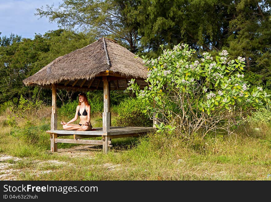 Woman doing yoga meditation in tropical gazebo