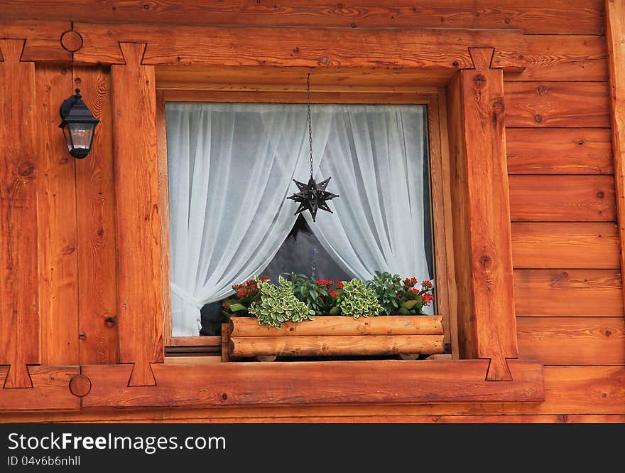 Detail of a mountain chalet wooden window . Flower vase and christmas decoration. Detail of a mountain chalet wooden window . Flower vase and christmas decoration