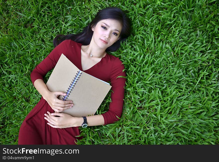 Woman lying on green grass with a book