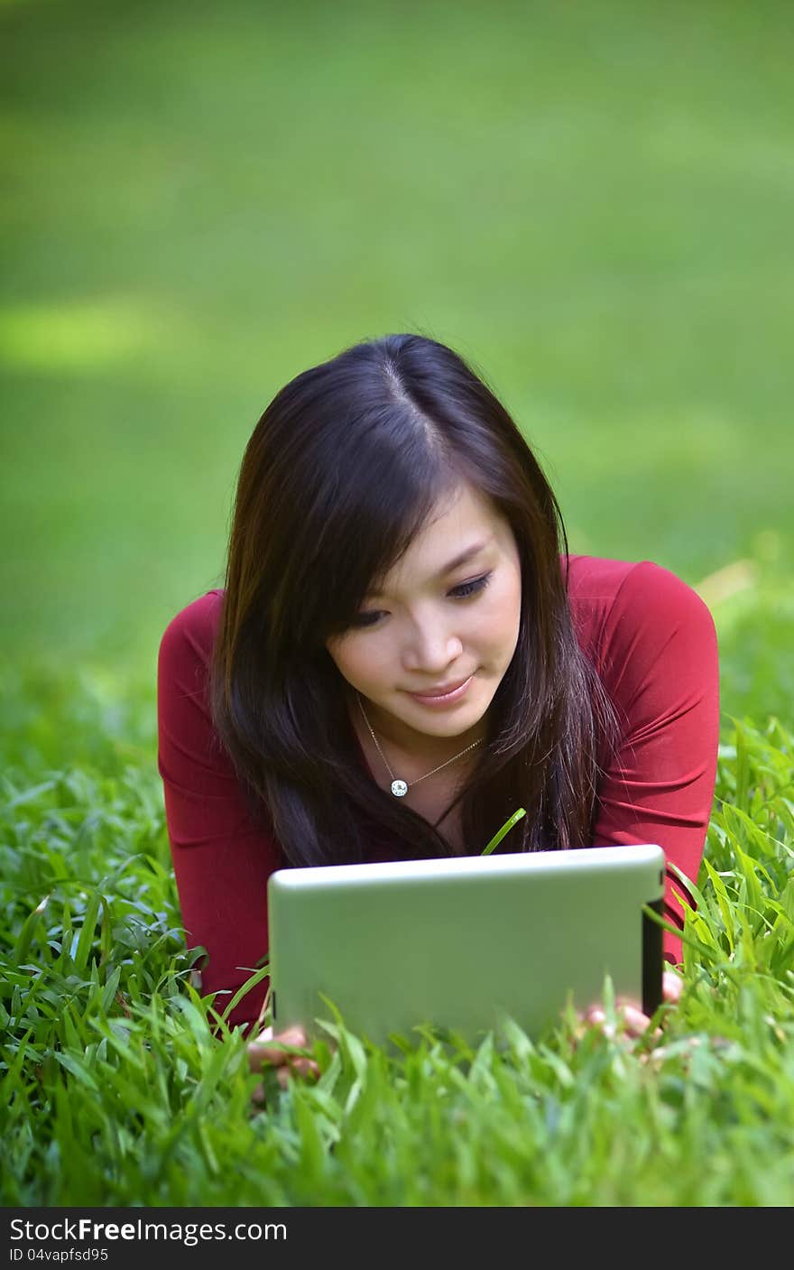 Pretty woman using tablet outdoor laying on grass