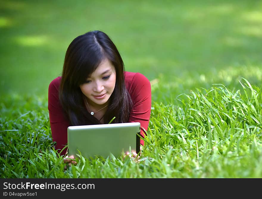 Pretty woman using tablet outdoor laying on grass