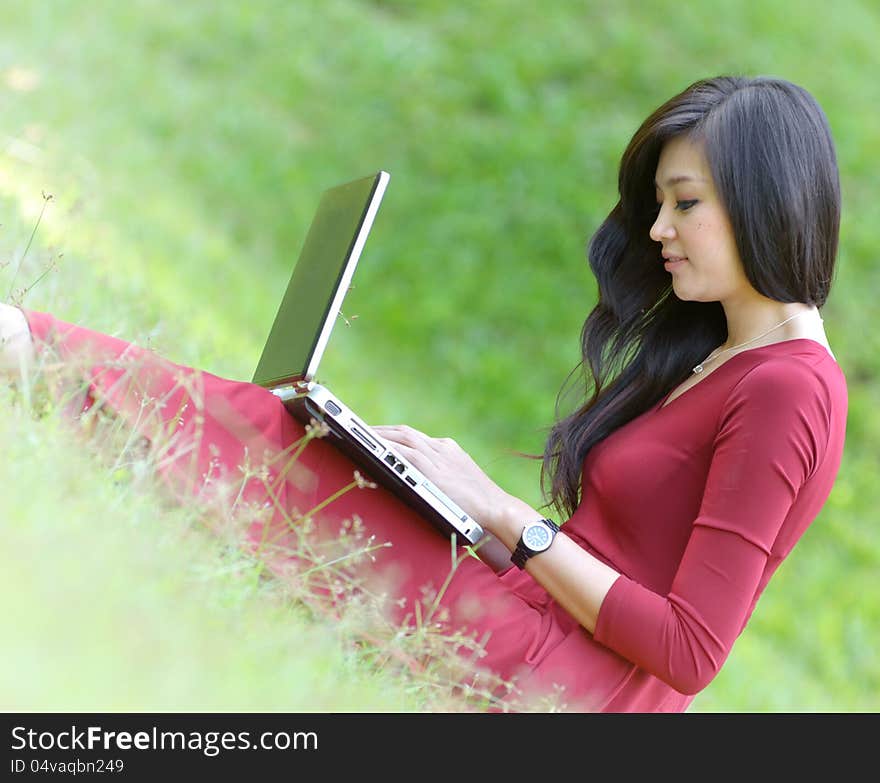 Pretty woman with laptop on green grass at the garden