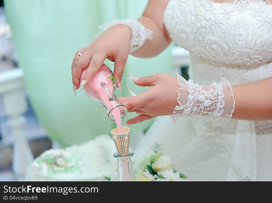 Beautiful bride's hands poured colored sand into a bottle. Beautiful bride's hands poured colored sand into a bottle