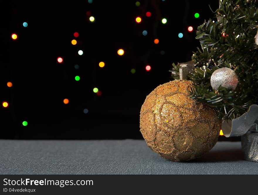 Golden ball under a decorated Christmas tree in the background colour of the lights