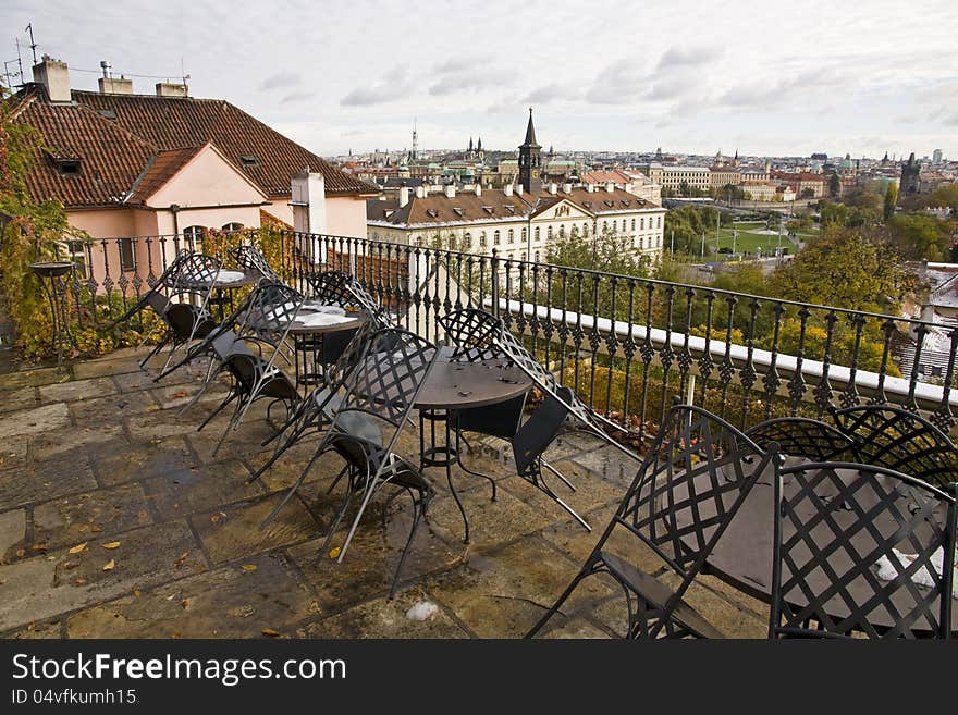 Outdoor seating with black tables and chairs in a restaurant near the prague castle in the czech republic, in the background are the roofs of the old town. Outdoor seating with black tables and chairs in a restaurant near the prague castle in the czech republic, in the background are the roofs of the old town