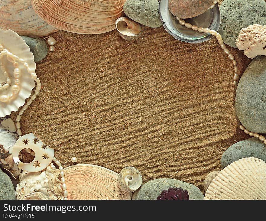 The decorated frame of shells and stones on the sand background. The decorated frame of shells and stones on the sand background