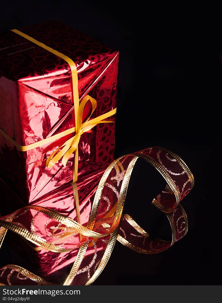 The gift in the red packaging ,delicate red ribbon on a black background with reflection