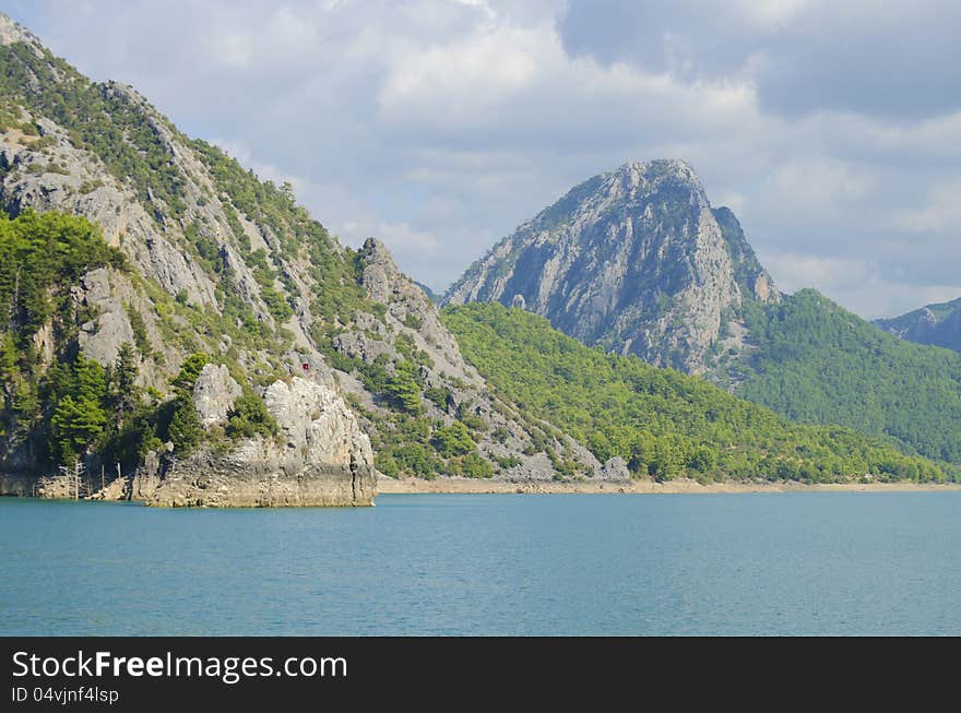 High mountains with growing trees and blue sky and lake. High mountains with growing trees and blue sky and lake