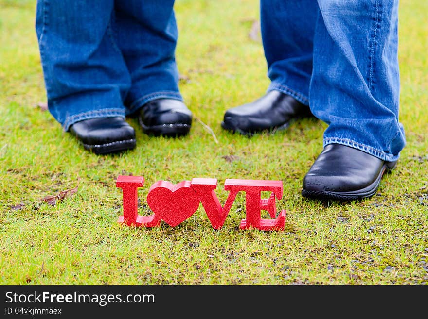 The feet of a couple with the word love in red on the green grass. The feet of a couple with the word love in red on the green grass.