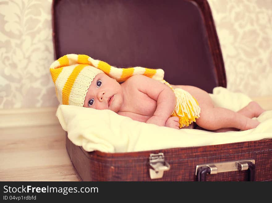 Naked baby in a warm hat is in the suitcase. Naked baby in a warm hat is in the suitcase