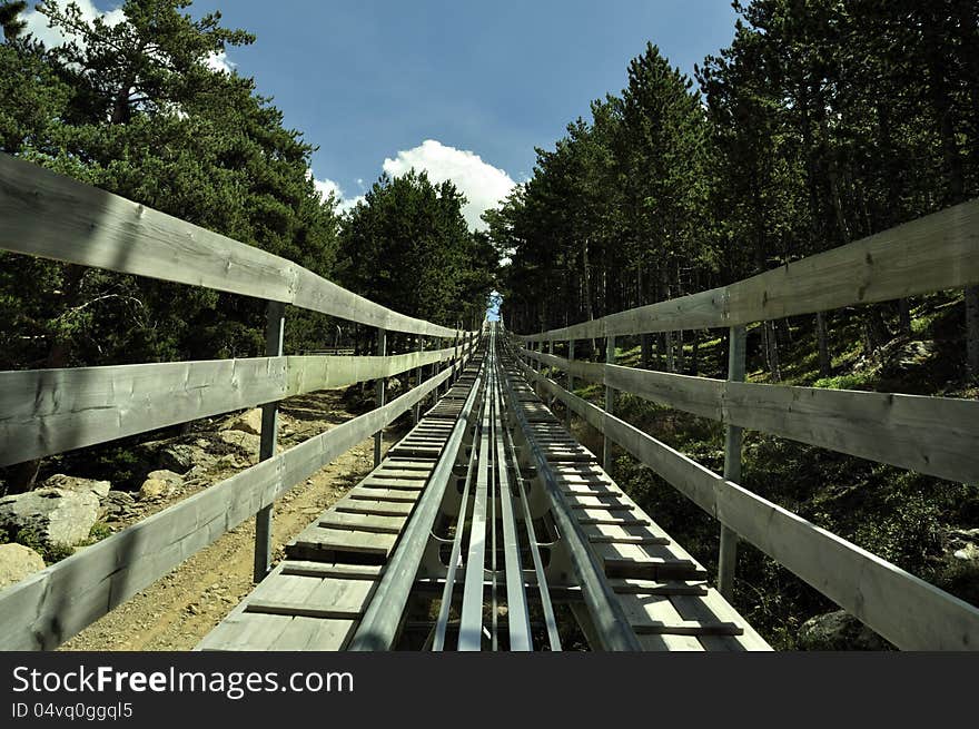 The track of an alpine roller coaster up to the peek, through the green forest in the summer. The track of an alpine roller coaster up to the peek, through the green forest in the summer