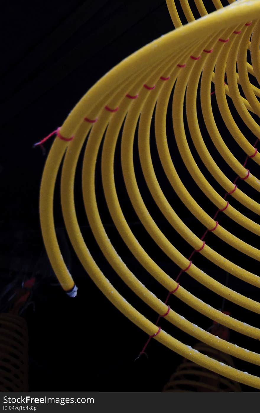 A close up of burning incense coils handing under the temple roof