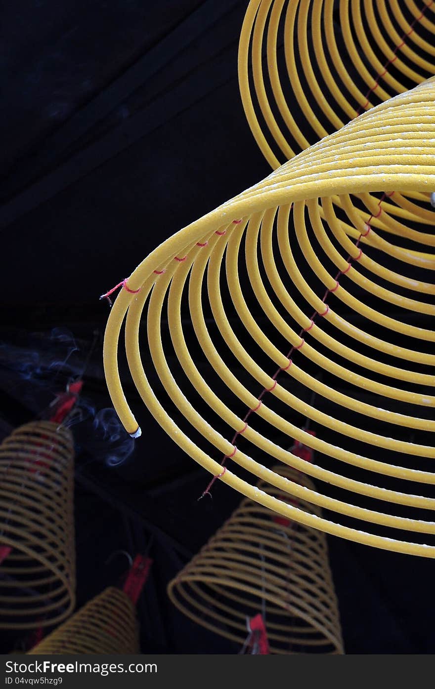 A close up of burning incense coils handing under the temple roof