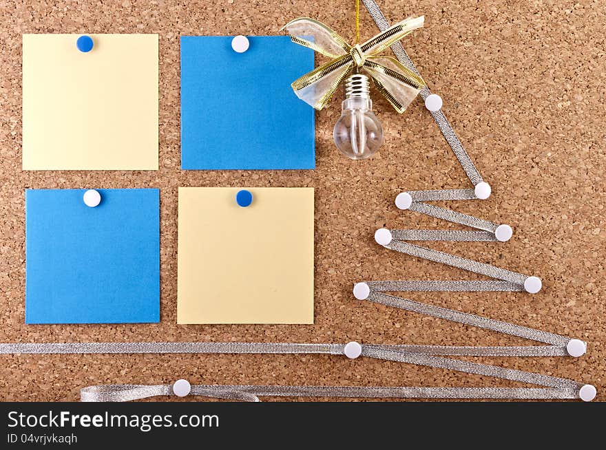 Corkboard with a New Year ideas empty paper notes, idea lamp with a festive bow and improvised silver Christmas tree. Corkboard with a New Year ideas empty paper notes, idea lamp with a festive bow and improvised silver Christmas tree.