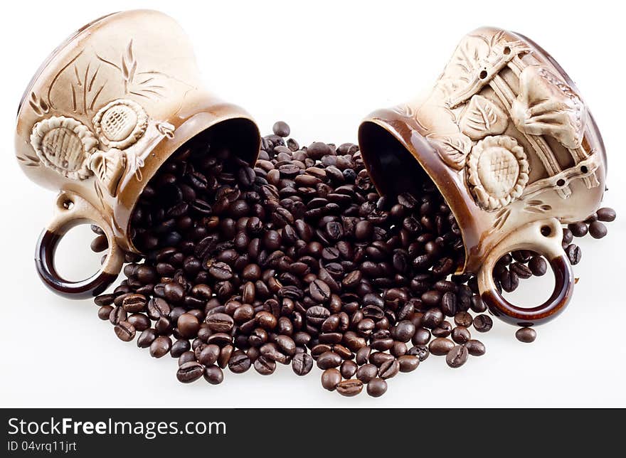 Hand made cups spill the coffee beans. Hand made coffee cups with spilt whole coffee beans closeup isolated on white.