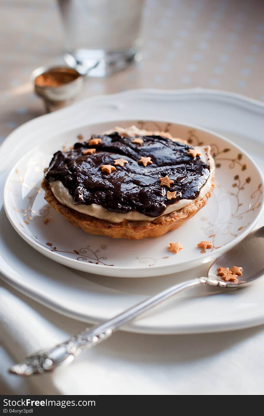 Christmas Tartlet Decorated with Chocolate, White Cream and Small Gold Asterisks on a White Plate. Christmas Tartlet Decorated with Chocolate, White Cream and Small Gold Asterisks on a White Plate