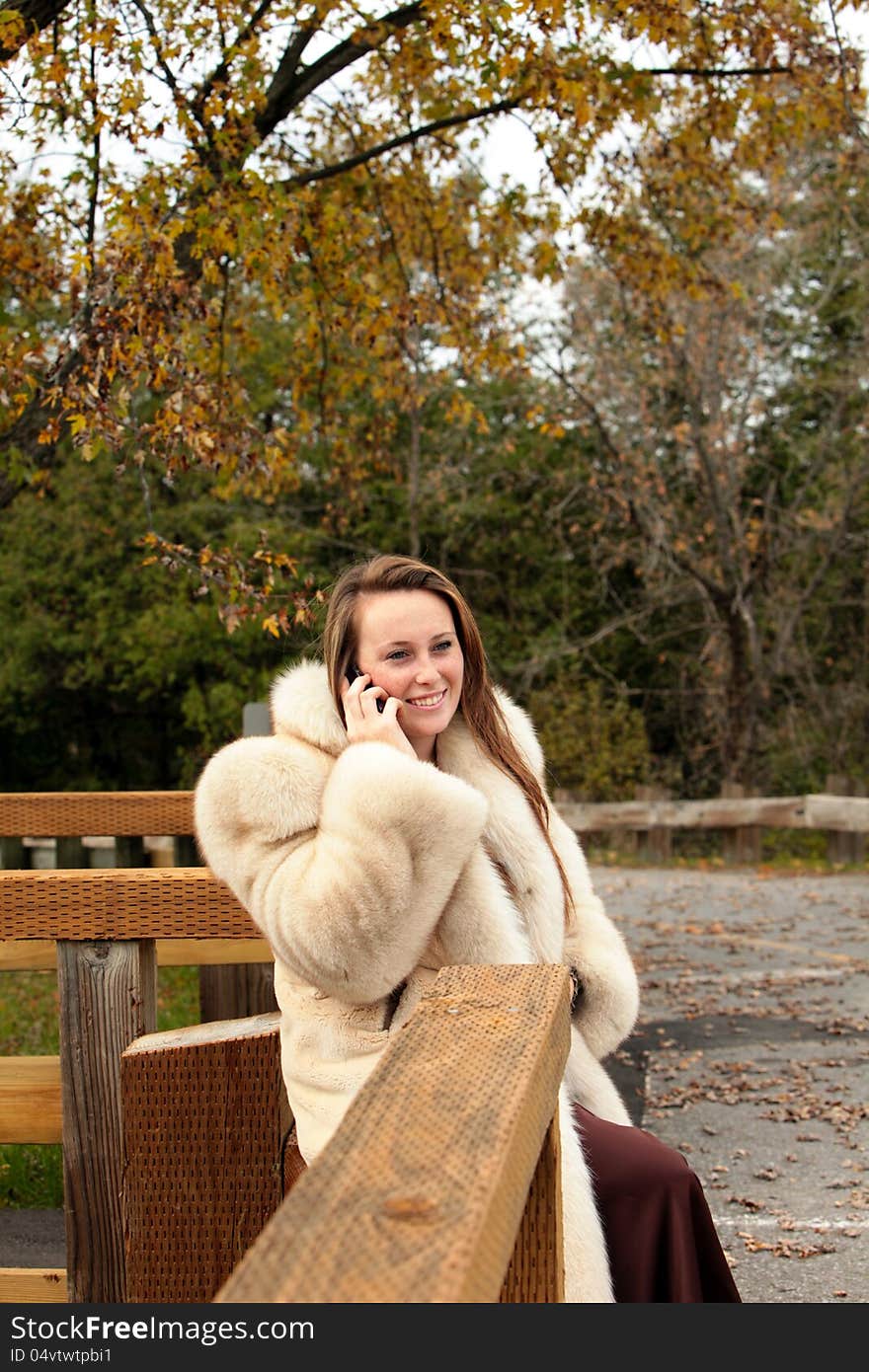 Pretty young girl talking on her cell phone wearing a formal gown and fur coat in late autumn. Pretty young girl talking on her cell phone wearing a formal gown and fur coat in late autumn.