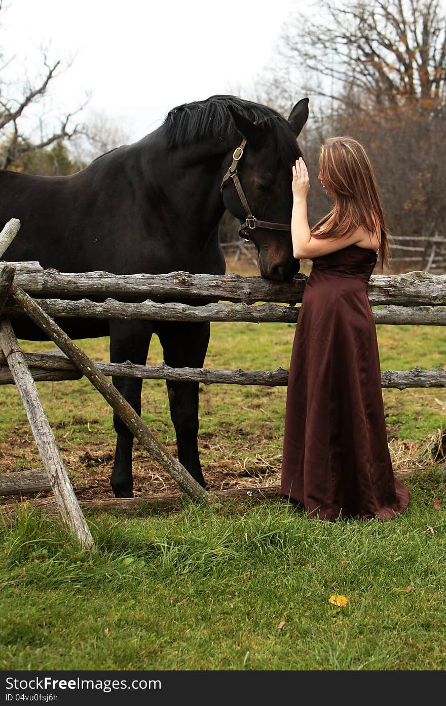 Pretty young woman in a long gown stands patting her horse in Autumn. Pretty young woman in a long gown stands patting her horse in Autumn.