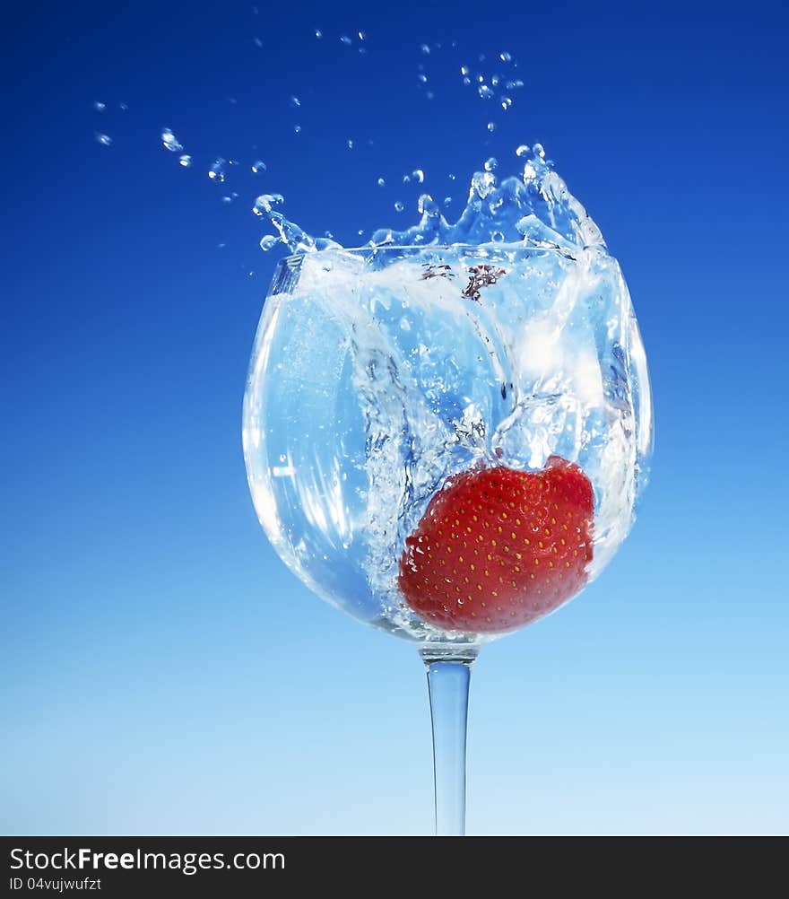 Close-up view of a large red strawberry splashing into a tall stemmed glass of refreshing clear liquid. Close-up view of a large red strawberry splashing into a tall stemmed glass of refreshing clear liquid