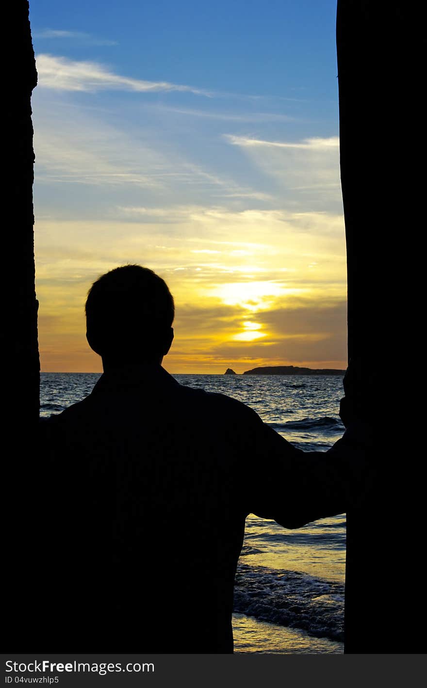 Silhouette of person standing between pillars and looking out to sea, an island, and a beautiful sunset. Silhouette of person standing between pillars and looking out to sea, an island, and a beautiful sunset.