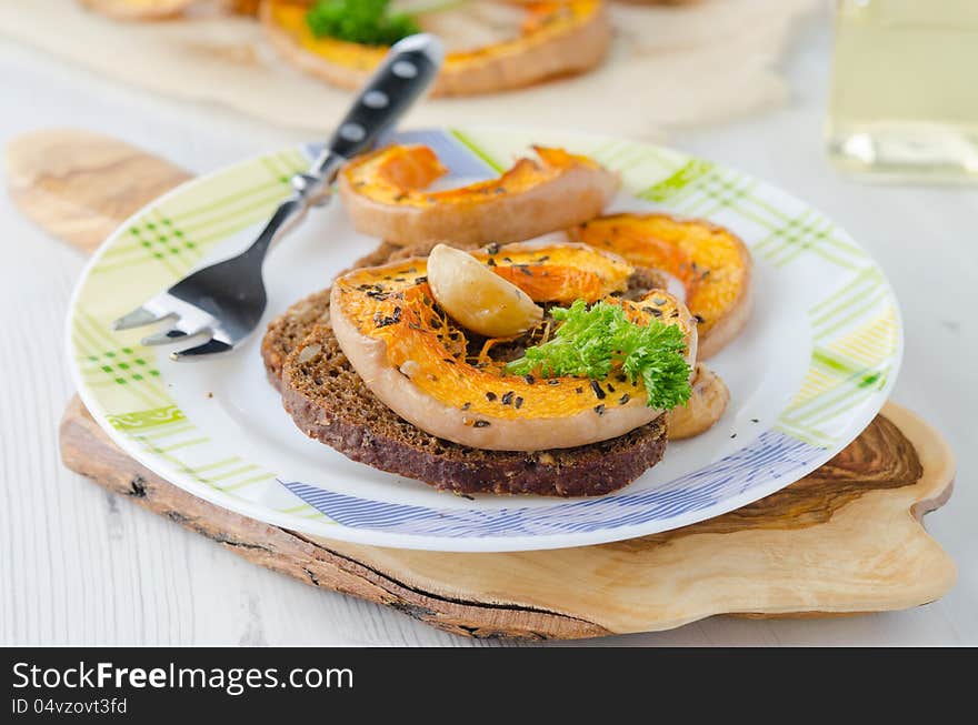 Appetizer - sliced ​​pumpkin baked with garlic and corn bread on a plate. Appetizer - sliced ​​pumpkin baked with garlic and corn bread on a plate