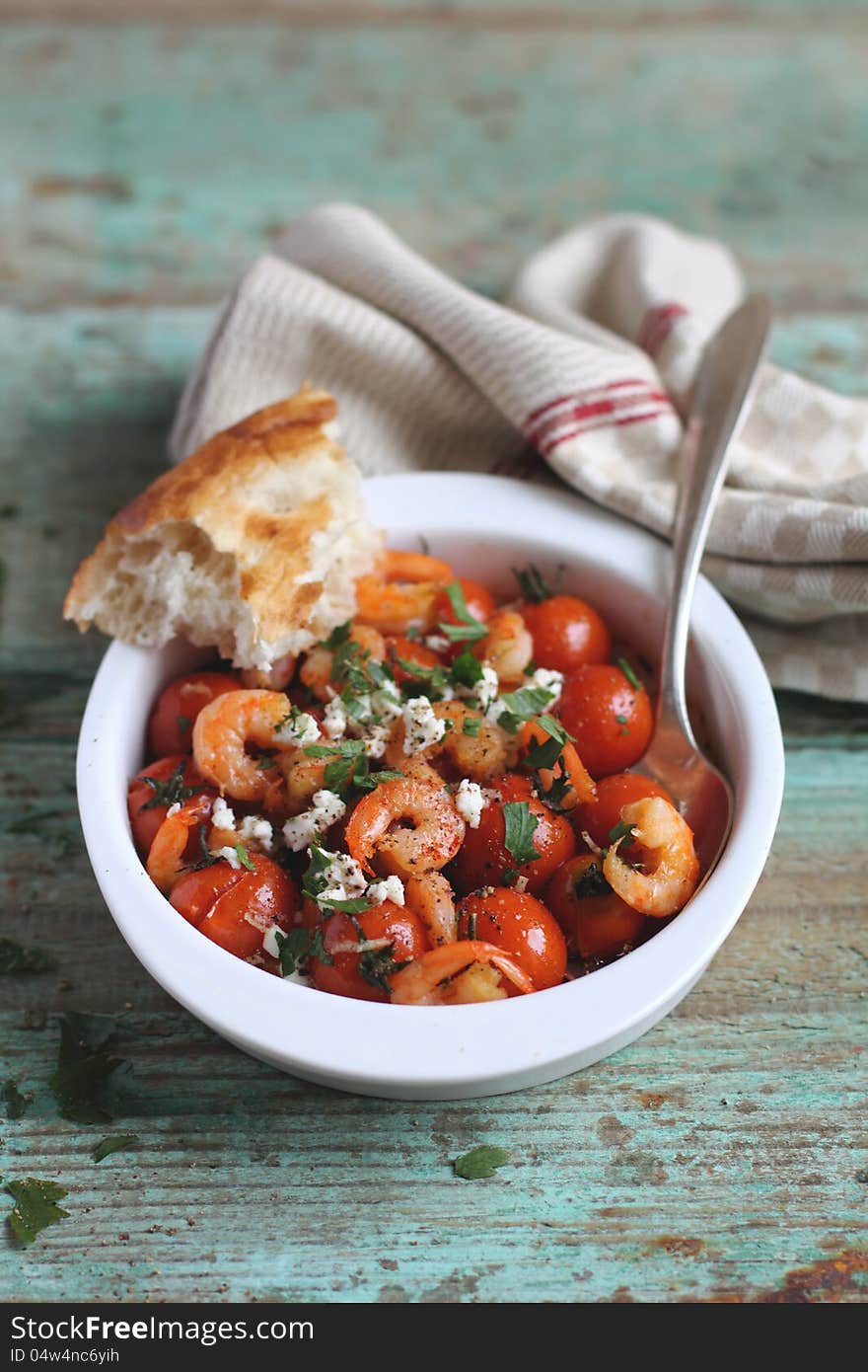 Baked shrimps and cherry tomatoes with feta cheese and fresh parsley in a baking dish with bread