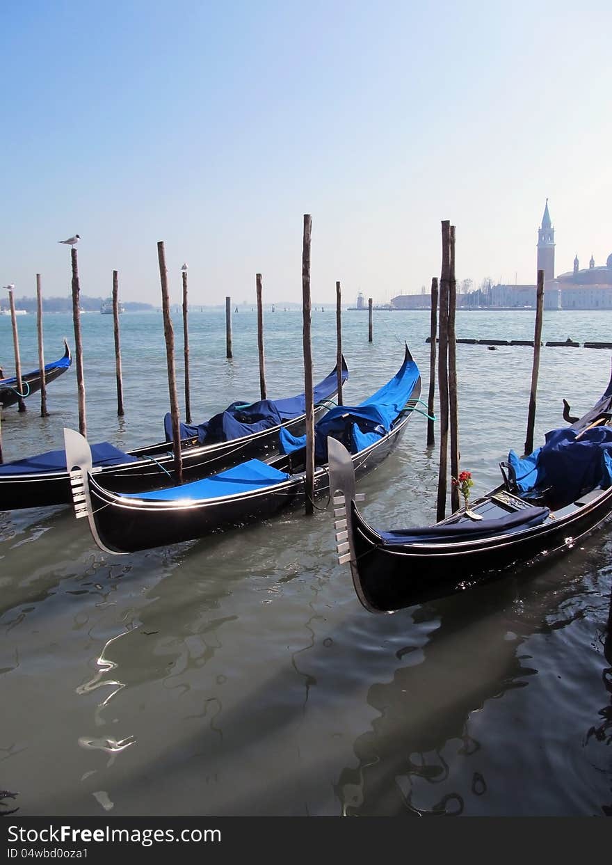 This image presents gondolas in Venice parked on a water canal. This image presents gondolas in Venice parked on a water canal.