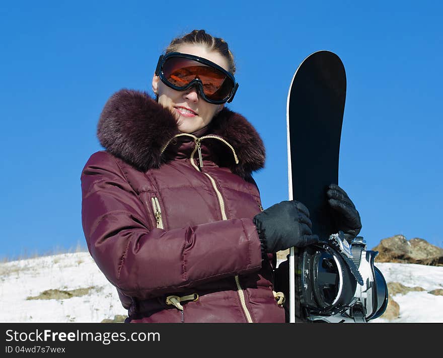 The young woman with a snowboard, in a helmet, in a ski glasses on the blue sky background