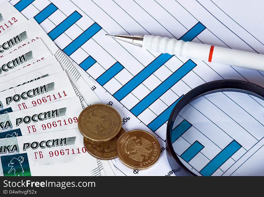 Metal and paper money, pencil and magnifying glass on a blue graph close-up