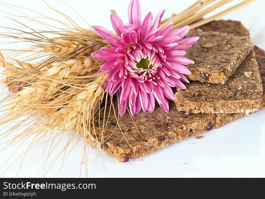 Whole wheat bread with ears of wheat and pink flower on a white background. Whole wheat bread with ears of wheat and pink flower on a white background