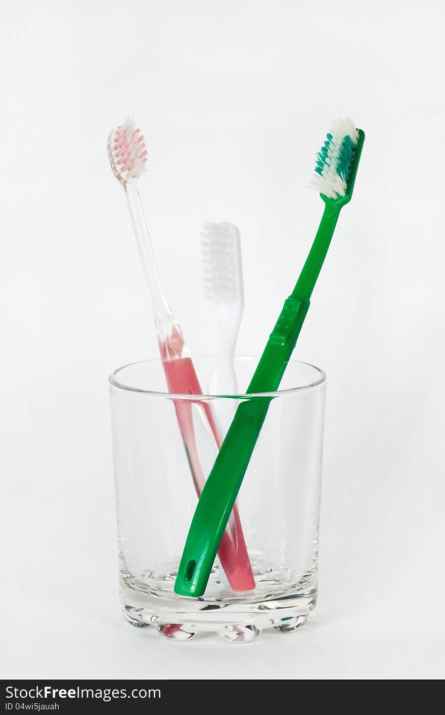 Three toothbrushes in a glass beaker on a white background