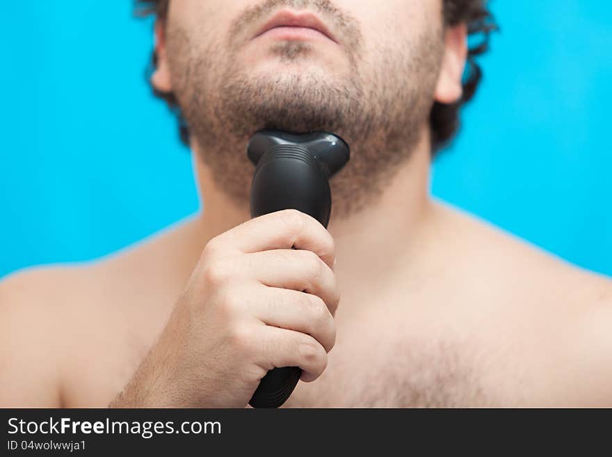 The man holds in a hand the electric razor at a chin, a half of the face. The man holds in a hand the electric razor at a chin, a half of the face