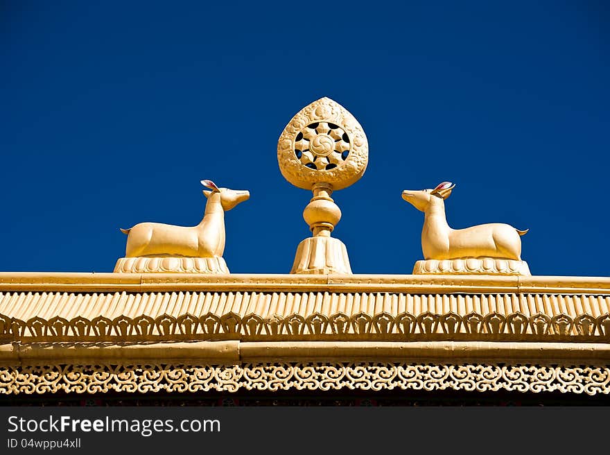 Tibetan Monastery Gates. Buddhist symbols: Dharma-wheel and deer on decorated roof under blue sky at Thiksey Gompa. India, Ladakh, Thiksey Monastery