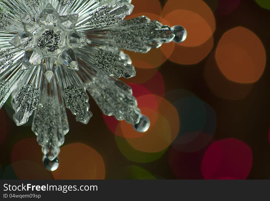 Silver snowflake Christmas ornament suspended from a pine bough against bokeh effect background