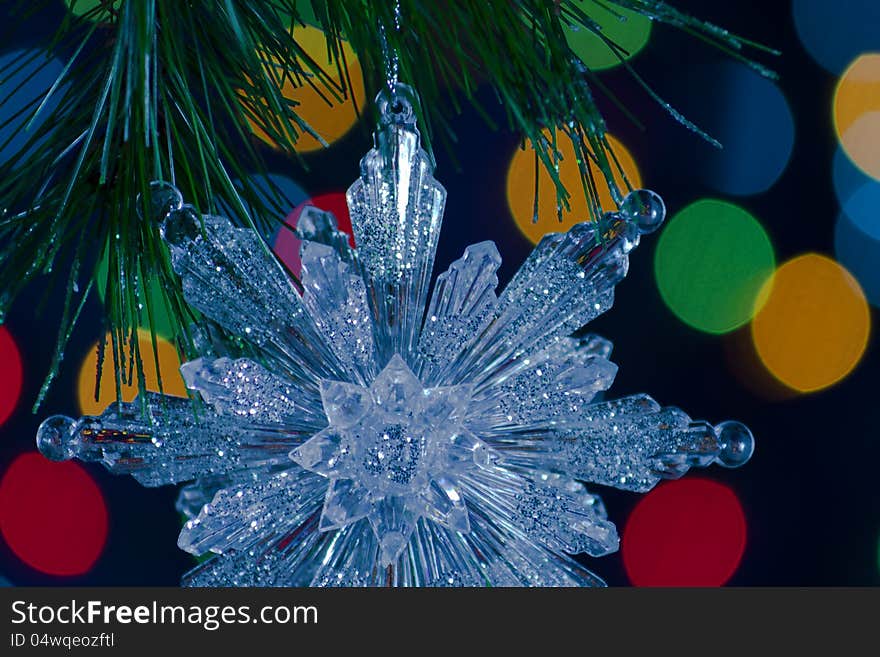 Snowflake Christmas ornament suspended from a pine bough against bokeh light background. Snowflake Christmas ornament suspended from a pine bough against bokeh light background