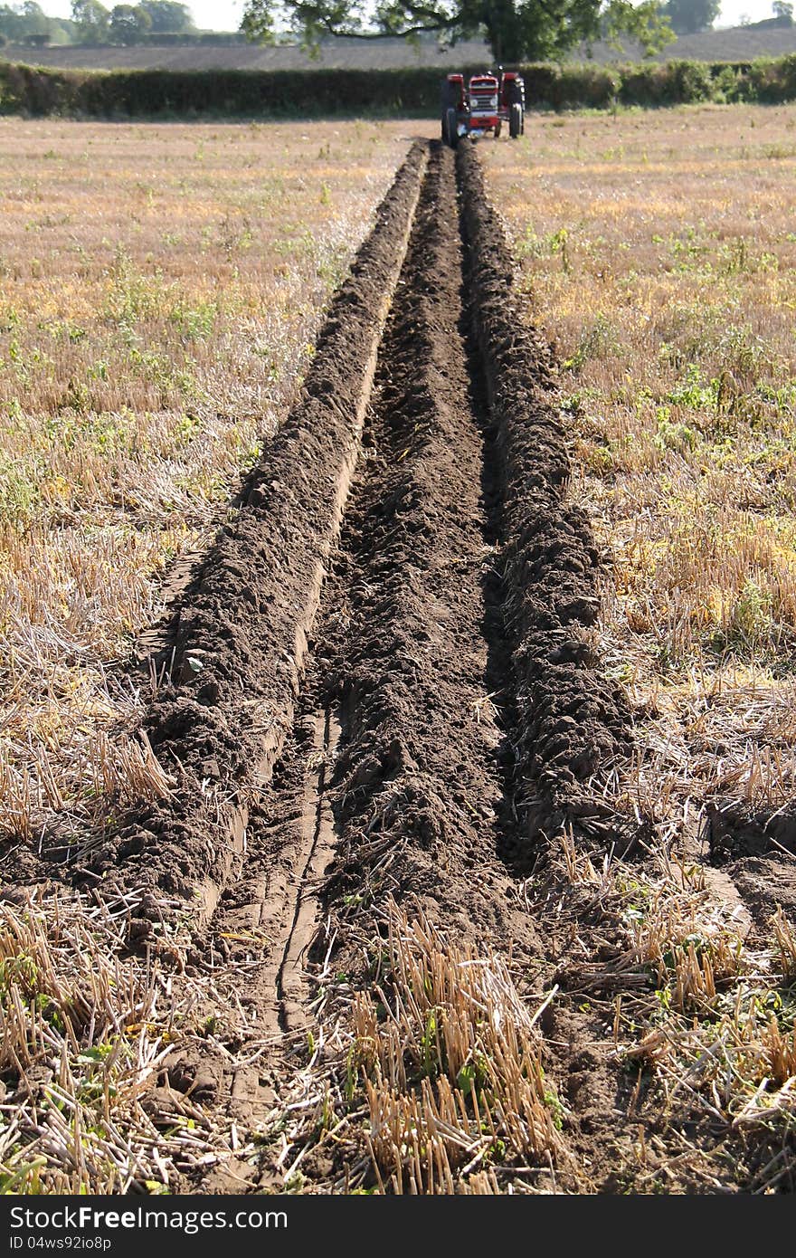 A Tractor at the Far End of a Ploughed Furrow in a Field.