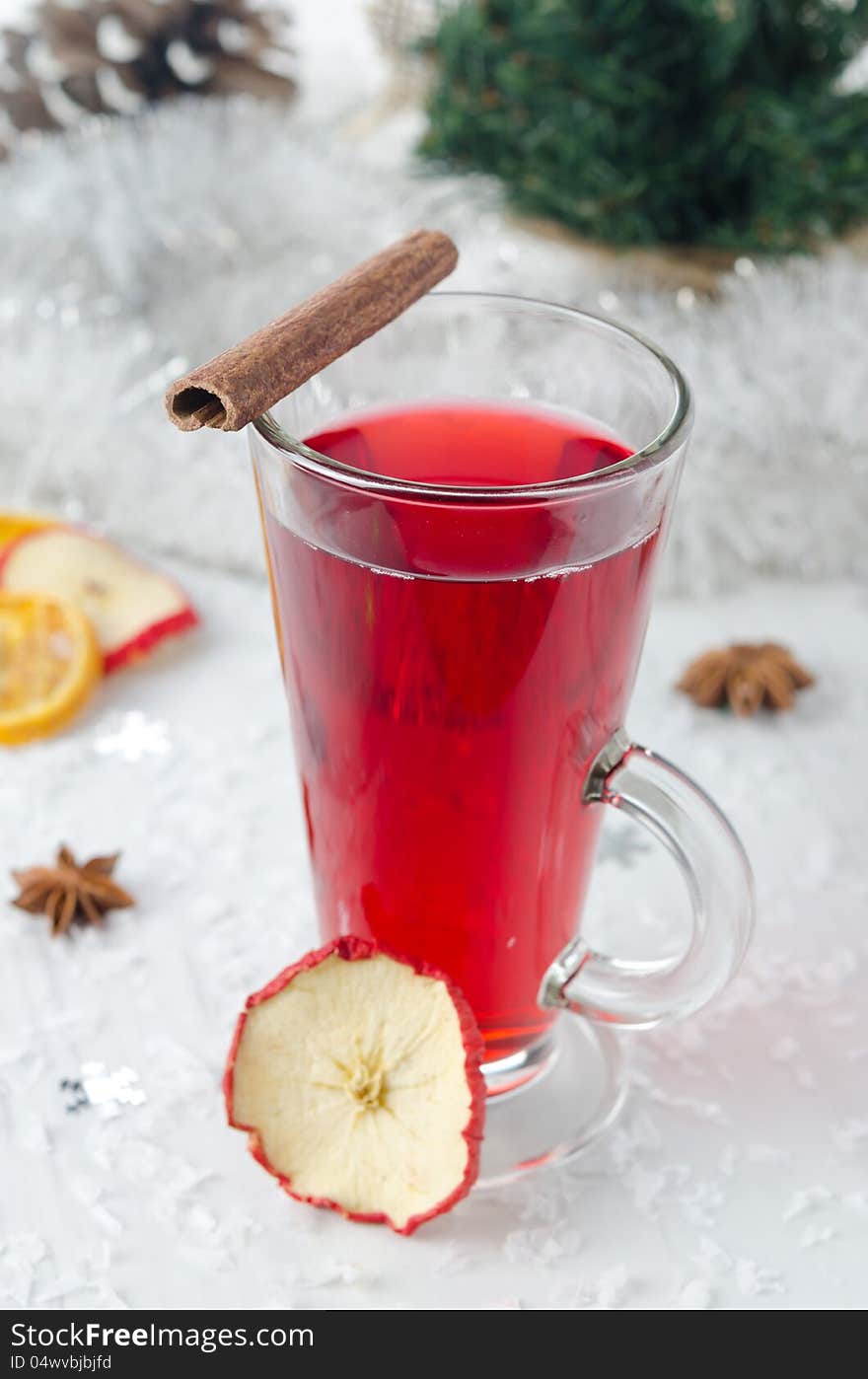 Mulled wine with cinnamon and spices in a glass glass, tinsel and Christmas tree in the background. Mulled wine with cinnamon and spices in a glass glass, tinsel and Christmas tree in the background