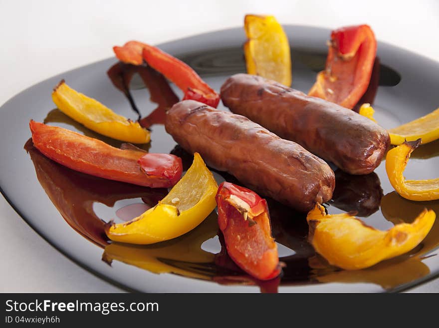 Grilled sausage and peppers on a black plate. close. Grilled sausage and peppers on a black plate. close