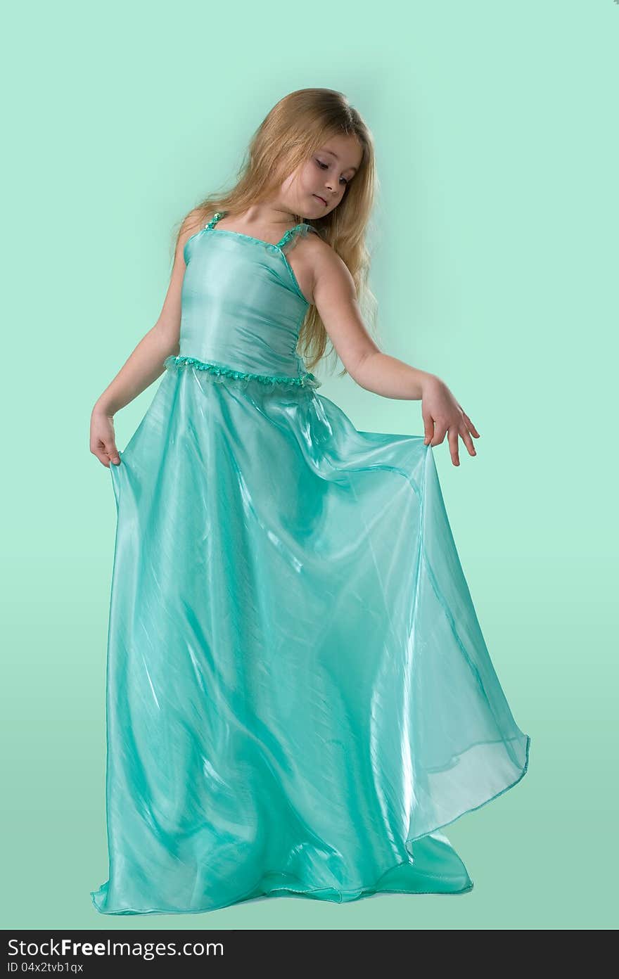 Full-length portrait of cute little girl in a smart long silk dress playfully posing in studio on light green background. Full-length portrait of cute little girl in a smart long silk dress playfully posing in studio on light green background