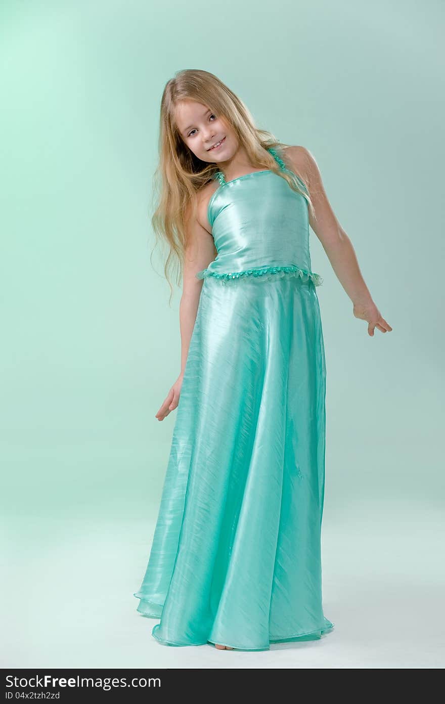 Full-length portrait of cute little girl in a smart long silk dress playfully posing in studio on light green background. Full-length portrait of cute little girl in a smart long silk dress playfully posing in studio on light green background