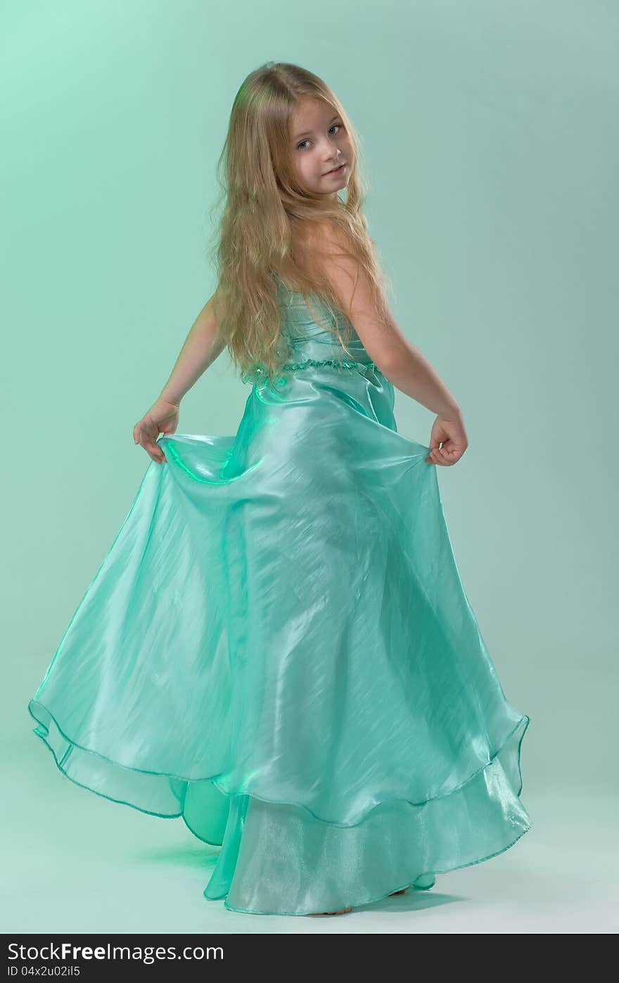 Full-length portrait of cute little girl in a smart long silk dress playfully posing in studio on light green background. Full-length portrait of cute little girl in a smart long silk dress playfully posing in studio on light green background