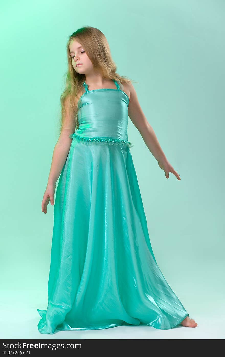 Full-length portrait of cute little girl in a smart long silk dress playfully posing in studio on light green background. Full-length portrait of cute little girl in a smart long silk dress playfully posing in studio on light green background