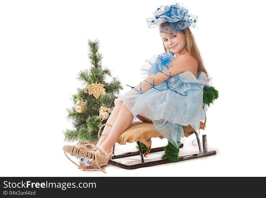 Portrait of a cute little girl in a beautiful dress and ornaments for the head against the Christmas tree and a sledge. Portrait of a cute little girl in a beautiful dress and ornaments for the head against the Christmas tree and a sledge