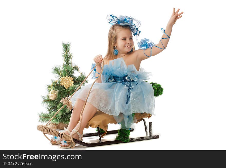 Portrait of a cute little girl in a beautiful dress and ornaments for the head against the Christmas tree and a sledge. Portrait of a cute little girl in a beautiful dress and ornaments for the head against the Christmas tree and a sledge