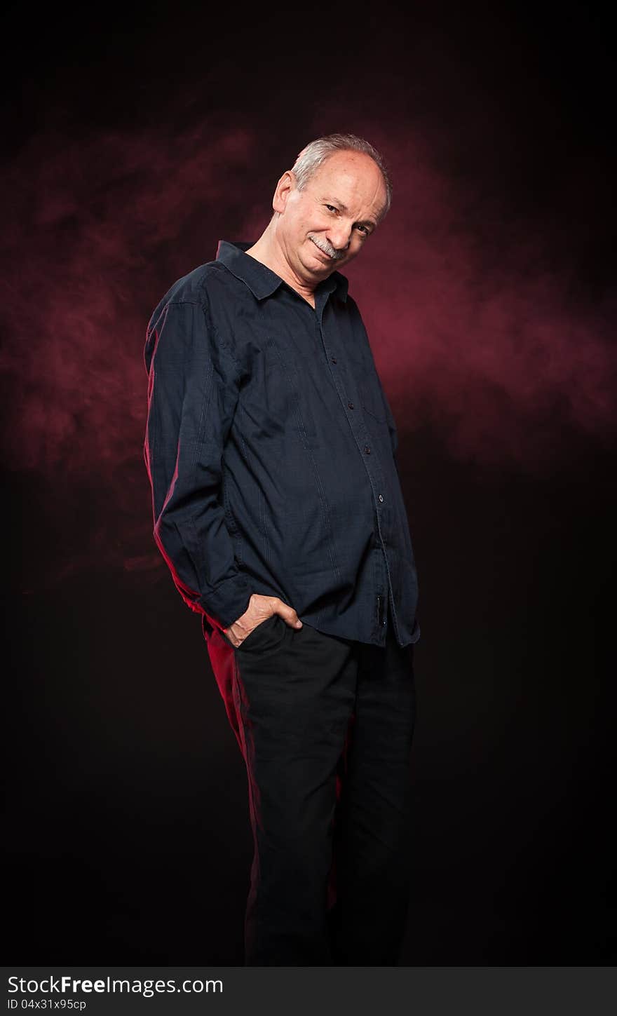 Elderly man in a black shirt standing on a dark background