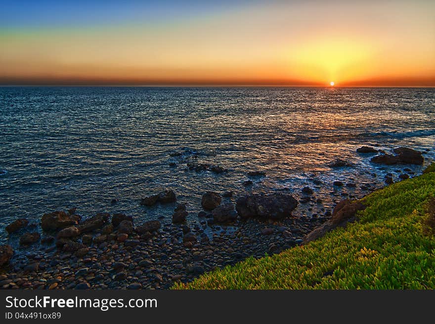 A beautiful panorama of a sunset on a calm sea, with a dark cloud on blue sky. A beautiful panorama of a sunset on a calm sea, with a dark cloud on blue sky.