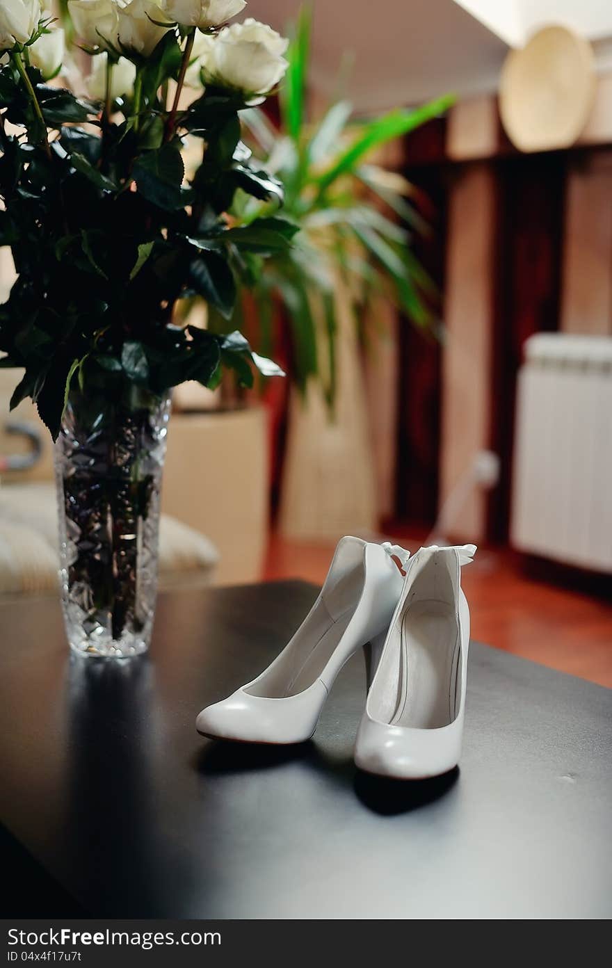 On the wooden floor are white shoes for the bride with dressing. On the wooden floor are white shoes for the bride with dressing