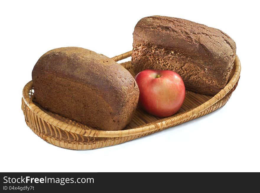 Two loaves of rye bread and an apple in a straw basket. Two loaves of rye bread and an apple in a straw basket